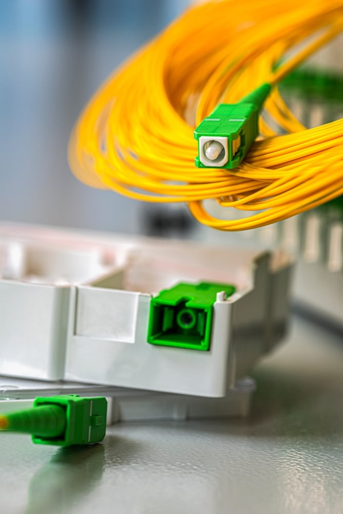 Connecteur Fibre Optique SC/APC Vert pour Raccordement FTTH Raccordement FTTH: Un connecteur fibre optique SC/APC vert et son câble jaune enroulé près du support de terminaison optique blanc.