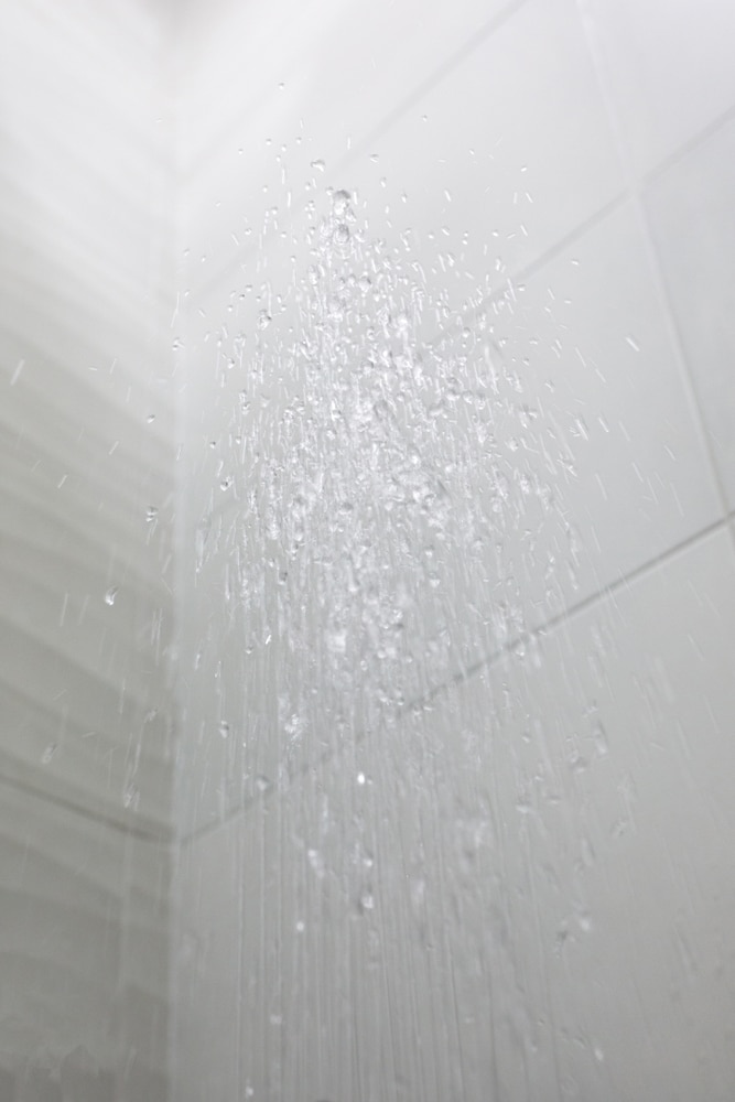 Douche : le puissant jet d'eau sur carrelage blanc. Gouttes d'eau cristallines jaillissant d'un jet de douche, avec un fond de carrelage de salle de bain blanc et lumineux.